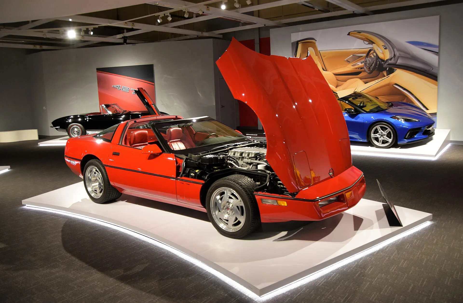 Red 1990 Chevrolet Corvette ZR-1 coupe on a museum display platform with its clamshell hood raised, showing the LT5 engine.