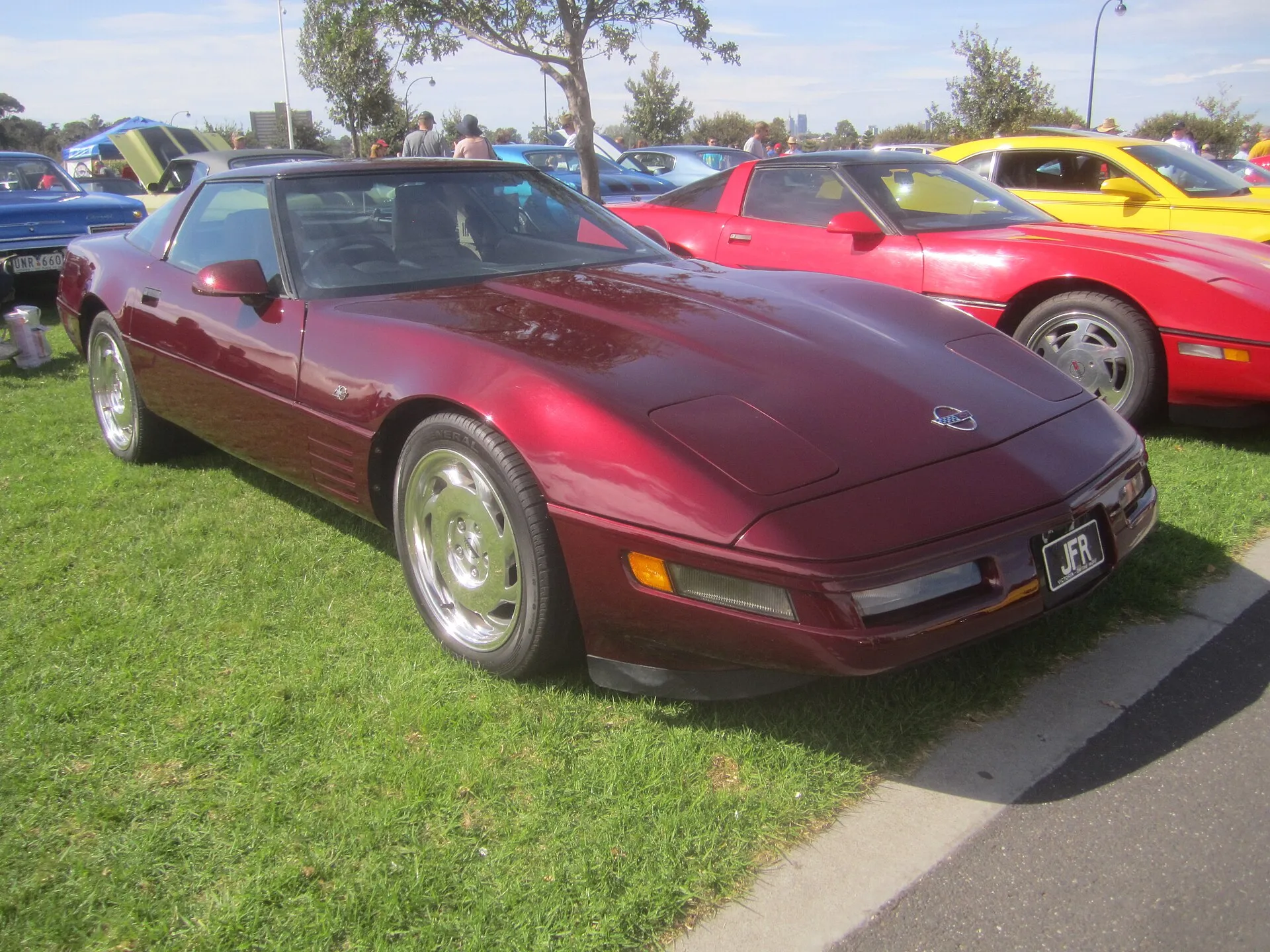 Ruby Red 1993 Chevrolet Corvette 40th Anniversary coupe with polished wheels, parked on grass at a car show.