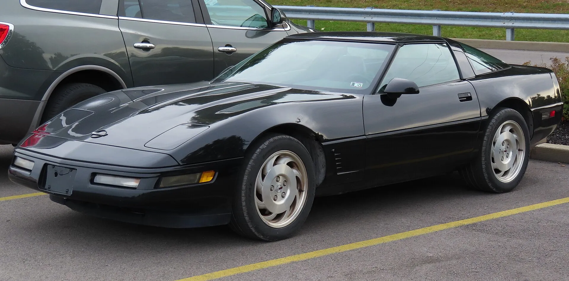 Black 1995 Chevrolet Corvette coupe in a parking lot, seen from the front left, with angled vents behind the front wheel.