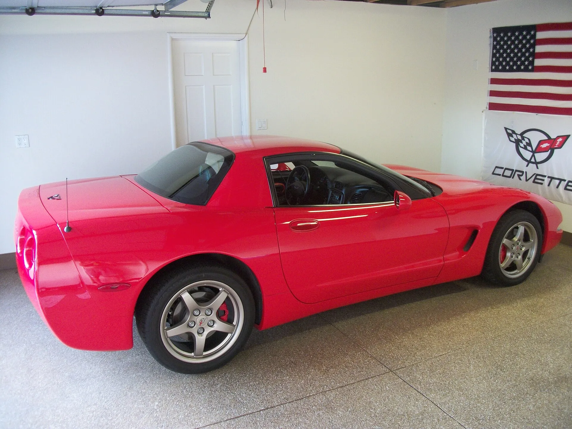 Red C5 Corvette hardtop, the fixed-roof model, parked in a garage and seen from the rear left.