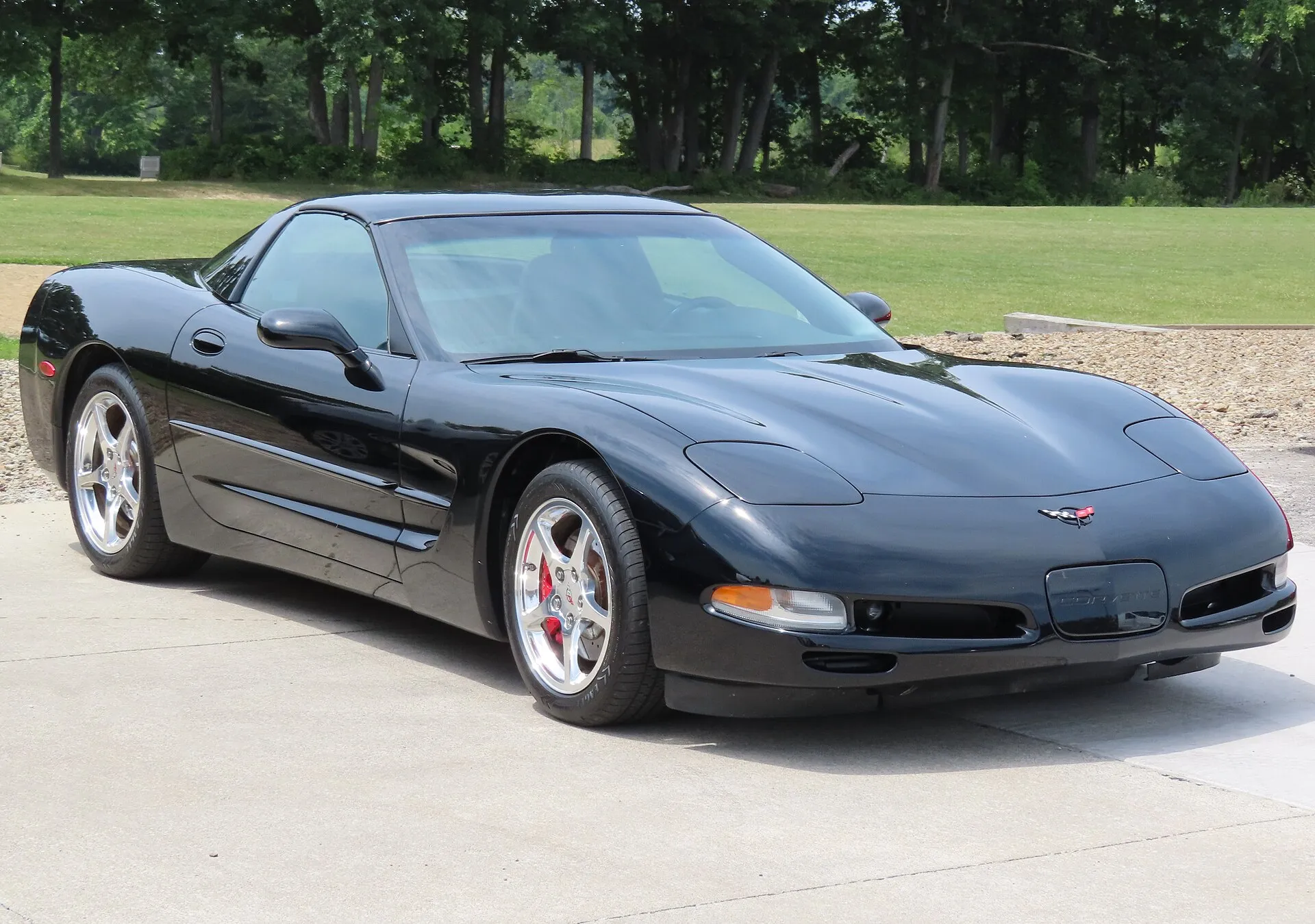Black 2004 Chevrolet Corvette C5 coupe parked on a concrete pad, seen from the front right, with polished five-spoke wheels and red brake calipers.