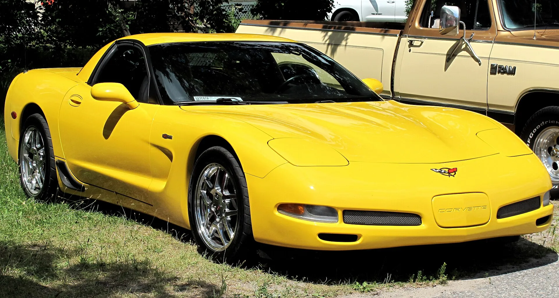 Millennium Yellow 2001 Chevrolet Corvette Z06 parked on grass beside a pickup truck, seen from the front right, with chrome-finish split five-spoke wheels and a Z06 badge on the front fender.