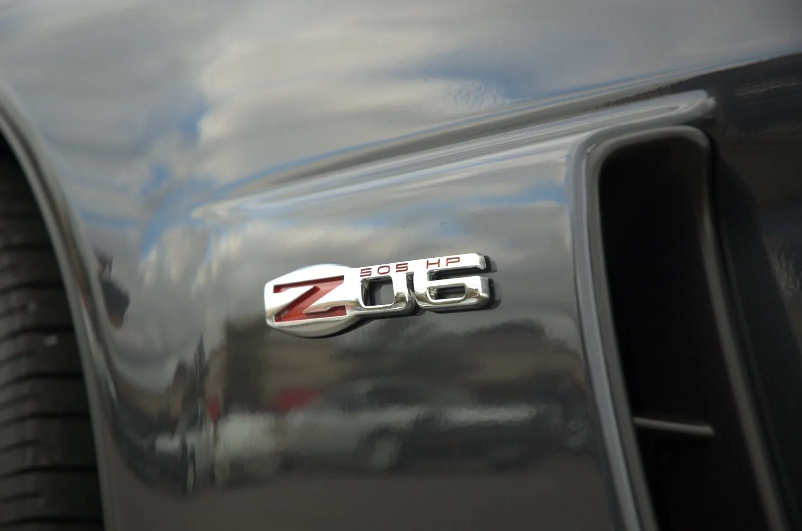 Close-up of a chrome Z06 badge with a red Z and the words 505 HP on the dark front fender of a C6 Corvette Z06, beside the fender vent.