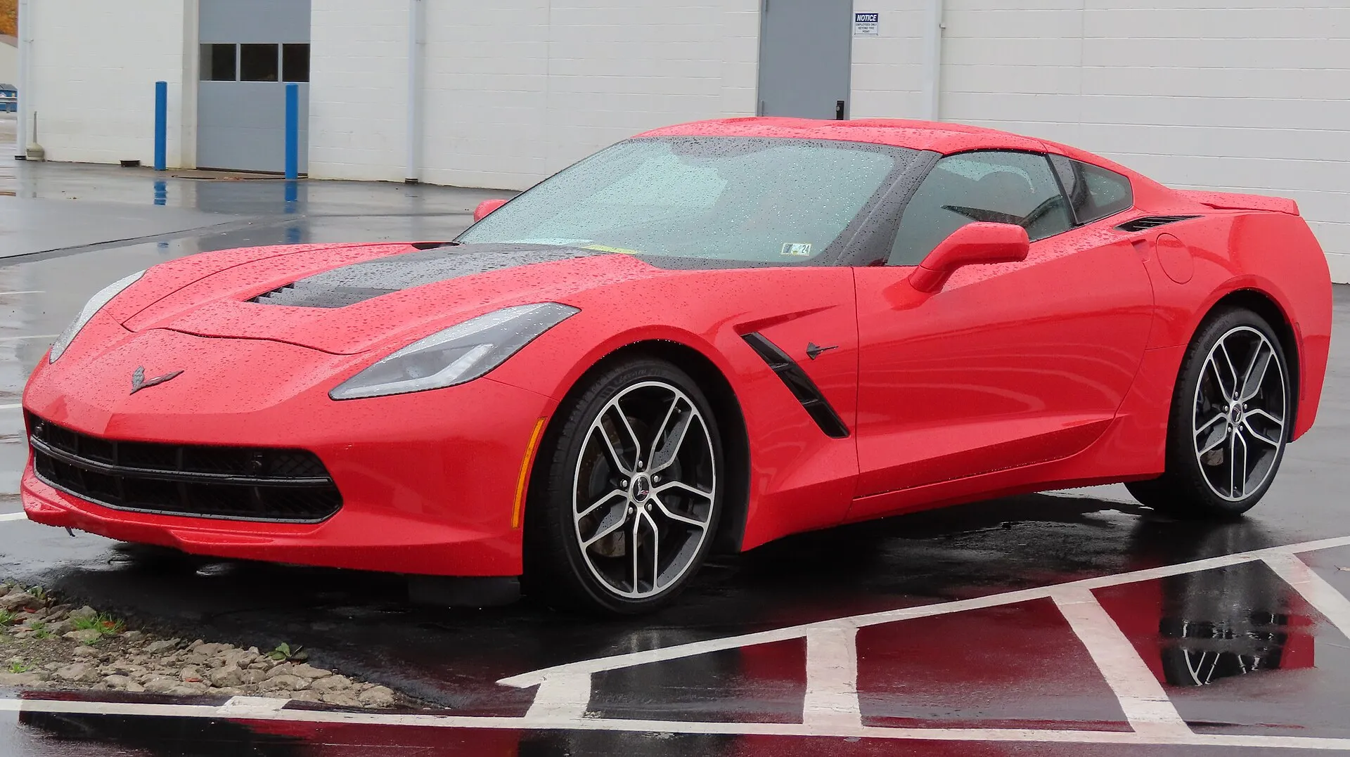 Red 2016 Chevrolet Corvette Stingray Z51 coupe parked on a wet lot, seen from the front left.