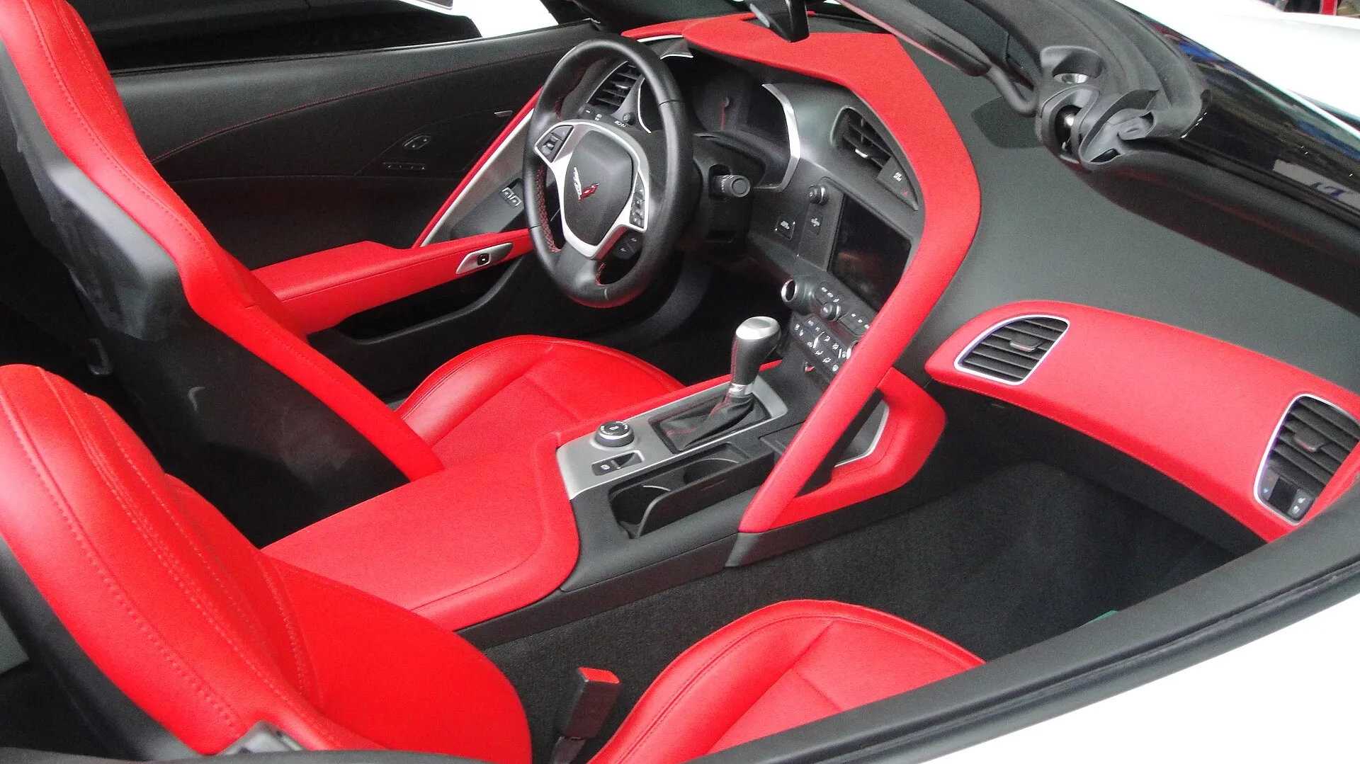 Red leather seats and red dashboard trim in a C7 Corvette Stingray with its top open, seen from the passenger side, with the automatic shift lever on the console.