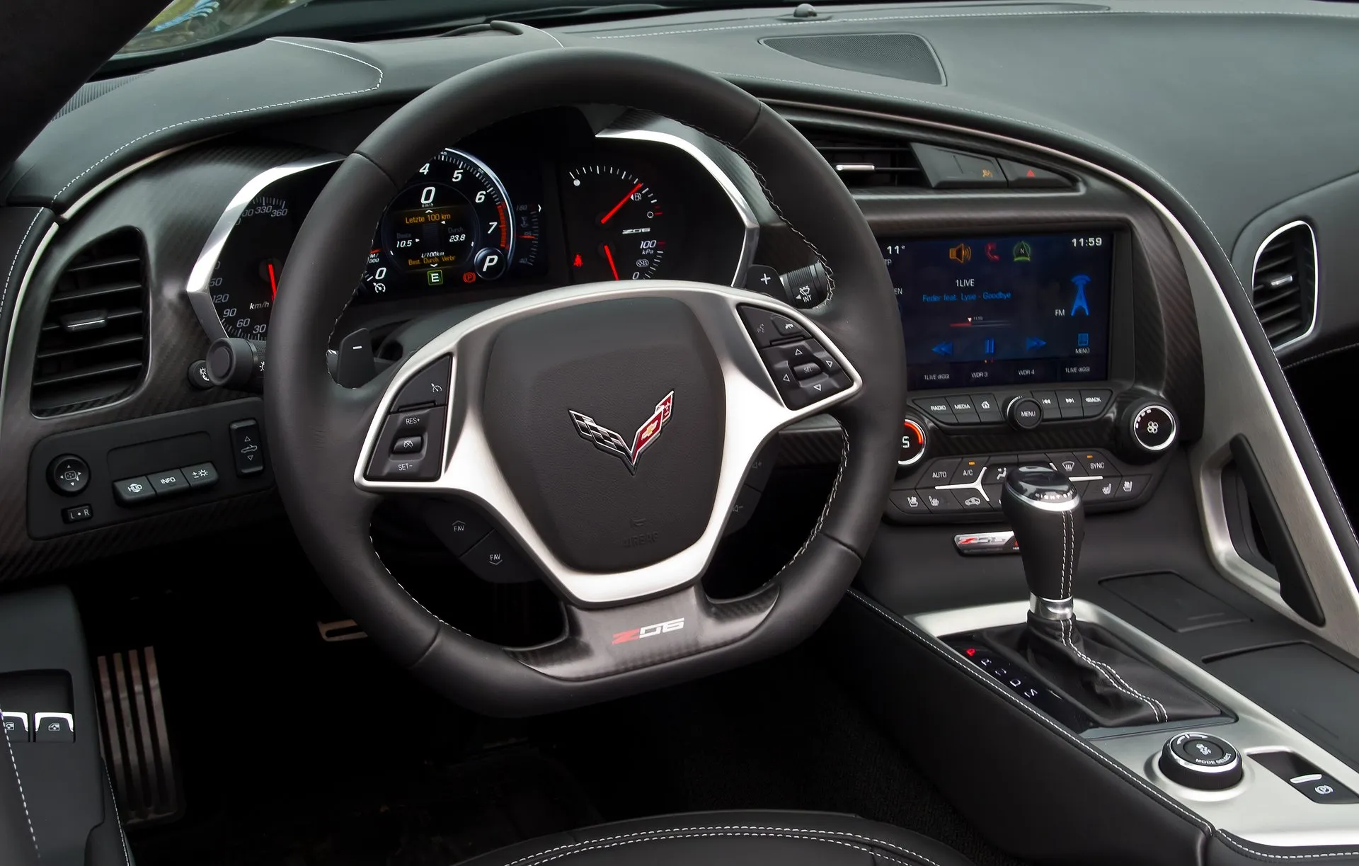 Cabin of a C7 Corvette Z06 convertible: a flat-bottomed steering wheel with a Z06 badge, the gauge cluster reading in kilometers per hour with P showing, the center touchscreen, and the eight-speed automatic's shift lever beside its lit P R N D M indicator.