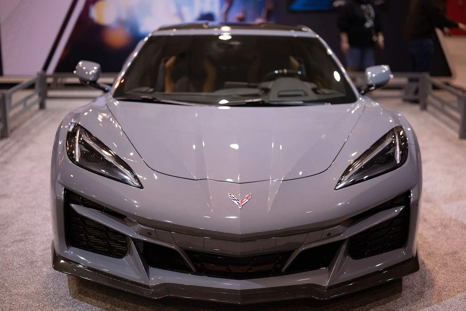 A gray C8 Corvette E-Ray seen head-on at an auto show, showing the long front hood over the front trunk.