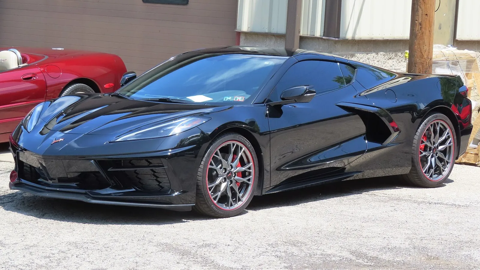 Black C8 Corvette Stingray coupe seen from the front left, parked outside a garage.