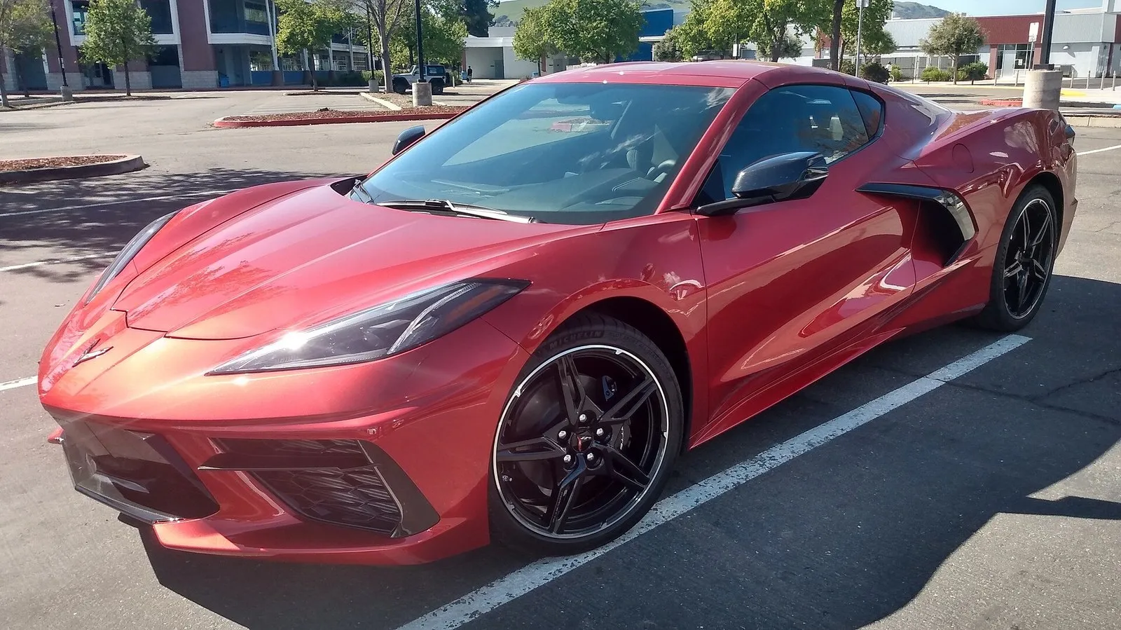 Red C8 Corvette Stingray coupe seen from the front left, parked in a parking lot, with its long front hood over the front trunk.