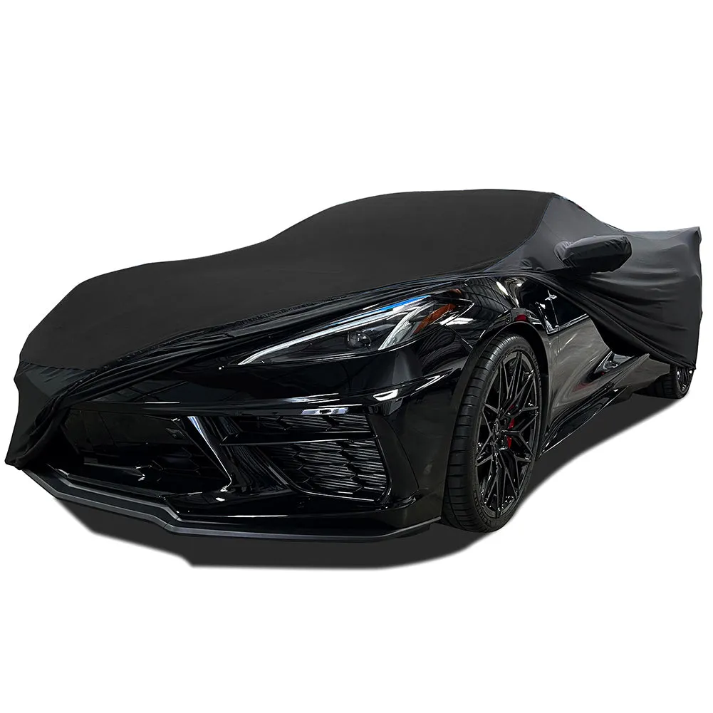 A black stretch satin cover pulled most of the way over a black C8 Corvette Stingray, leaving the front bumper, one headlight and the front wheel uncovered.